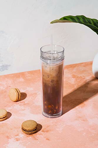 Iced coffee in a clear tumbler with macarons on a peach surface.